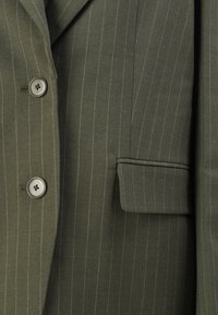 Veste de costume à rayures vert foncé avec un design à un bouton, deux boutons ronds et une poche plaquée sur le côté gauche.