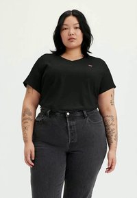Tricou negru cu gât în V, cu mâneci scurte, realizat dintr-un material moale. Purtați cu blugi închiși la culoare, cu talie înaltă, având detalii de cusătură subtile.
