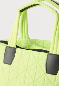 Τσάντα ώμου σε ανοιχτό πράσινο χρώμα με ραμμένες επενδύσεις, μαύρο φερμουάρ και μαύρα δερμάτινα ενισχυτικά στη βάση των χερουλιών, σε λευκό φόντο.