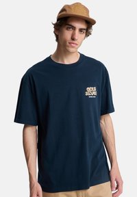 Μπλε ναυτικό βαμβακερό t-shirt με κοντά μανίκια και άνετη εφαρμογή, με μικρό λογότυπο γραφικών σε κρεμ χρώμα στο αριστερό στήθος.