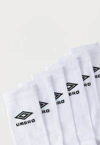 Άσπρες βαμβακερές κάλτσες με ραβδωτή υφή, με μαύρο λογότυπο "UMBRO" και διαμάντι μοτίβο. Τακτοποιημένες σε σειρά, έξι ζευγάρια ορατά.