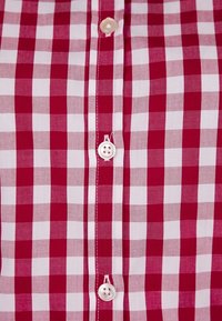 Camicia a quadri rossi e bianchi con colletto abbottonato di fronte, dotata di bottoni bianchi e realizzata in un tessuto leggero e testurizzato.
