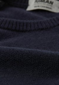 Suéter de lana Navy con cuello acanalado, que presenta una textura suave y una etiqueta cosida en el cuello. La vista en primer plano revela fibras finas.