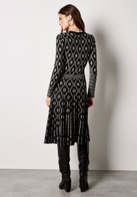 Czarna i biała sukienka z długim rękawem z wzorem diamentowym, dopasowanym gorsetem oraz rozkloszowaną spódnicą, wykonana z teksturowanej tkaniny.