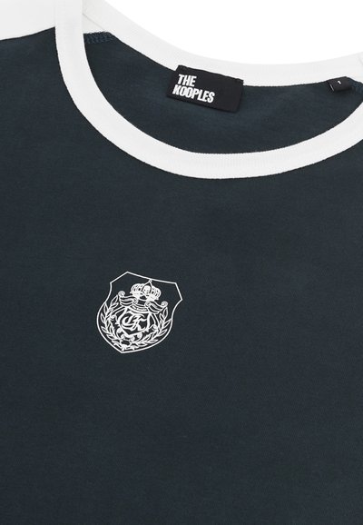 Schwarzes T-Shirt mit weißem Kragen, präsentiert ein Wappen-Logo in weißer Stickerei. Hergestellt aus weichem Material, lässiger Schnitt und glatte Textur.