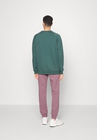 Grön sweatshirt med ribbad mudd och nederkant, tillsammans med rosa joggers med ankelmudd, bärs med vita träningsskor.