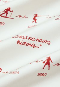 Tkanina tekstylna z białym tłem, na którym znajdują się czerwone grafiki sportowców oraz lata (1964, 1980, 2010, 2012) i cytat.