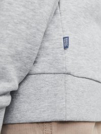 Sivi dukserica napravljena od meke mješavine pamuka, s rebrastim donjim rubom i manžetama, s malom plavom etiketom koja prikazuje "JACK & JONES" sa strane.