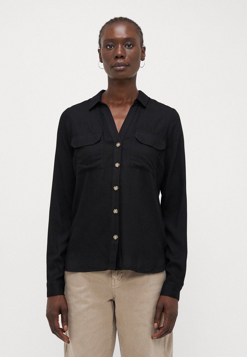 Chemise noire à manches longues avec col, deux poches poitrine et boutons dorés, fabriquée dans un tissu lisse et léger.
