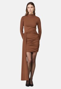 Braunes langärmliges Kleid mit geraffter Textur am Oberteil, einem drapierten seitlichen Detail und einem engen Schnitt, kombiniert mit schwarzen Absätzen.