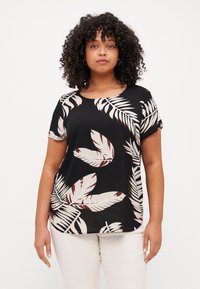 Schwarzes Kurzarmoberteil mit einem großen creme- und braunfarbenen Blattmuster, runder Halsauschnitt und weicher Stofftextur. Kombiniert mit hellen Hosen.