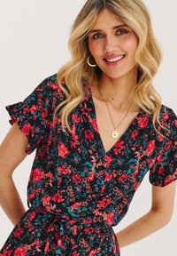 Černé květinové šaty s červenými a zelenými vzory, krátké volánkové rukávy, výstřih ve tvaru V a detaily s tkaným pasem. Nosit zlatý přívěsek na krku.