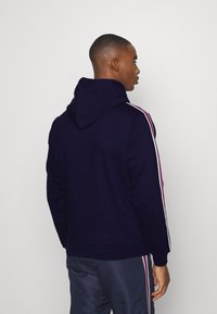 Felpa blu navy con cappuccio, caratterizzata da righe laterali bianche e rosse. Realizzata in materiale morbido, ha una vestibilità comoda con polsini e orlo a costine.
