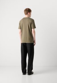 Tricou scurt cu mânecă în verde măsliniu, asociat cu pantaloni negri largi. Îmbrăcămintea are o siluetă relaxată și un design simplu.