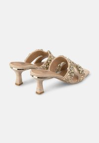 Mules beige con tacchi alti e cinturini trasparenti decorati con cristalli. Punta quadrata e tessuto testurizzato; tacco a blocco piccolo e robusto.