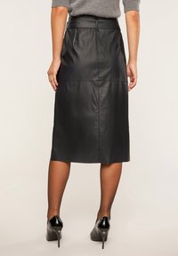 Musta nahkainen midihame, jossa on suora leikkaus, näkyvät saumat ja sileä pinta. Yhdistetty mustiin korkokenkiin.