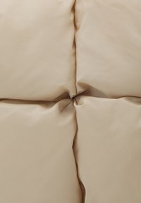 Literie matelassée beige avec une finition mate et lisse, présentant un nœud central froncé et une texture douce et moelleuse.