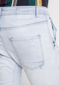 Světle modré džíny z denimu s vybledlou texturou, s jednou zadní kapsou s malou trhlinou a vysokým pasem.