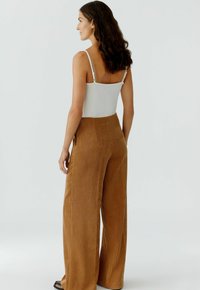 Witte mouwloze top met verstelbare bandjes, gecombineerd met hoge taille, wijde, gestructureerde bruine corduroy broek.