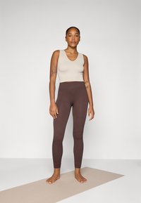 Bež ribidega top, mille juurde on sobitatud pruunid ribidega kõrge talje legginsid, mõlemad hästi istuvad, minimalistlik disain, neutraalses taustas.