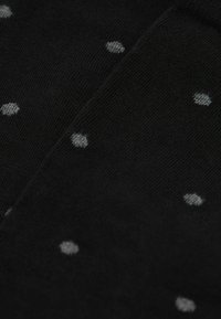 Svarta strumpor med stickad struktur och mönstrade med små grå prickar, jämnt fördelade över tyget.