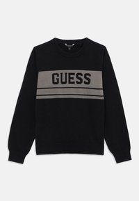 Svart strikkegenser med en grå horisontal stripe og "GUESS" logo i fete svarte bokstaver over brystet. Rund halslinning og ribbestrikkede mansjetter.