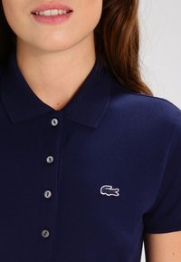 Navy polo shirt with a buttoned placket, textured cotton fabric, and a small white embroidered crocodile logo on the left chest.