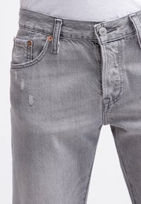 Grå denimjeans med en avslappnad passform, med subtil slitage på framsidan, kopparnitar och en klassisk knappstängning.