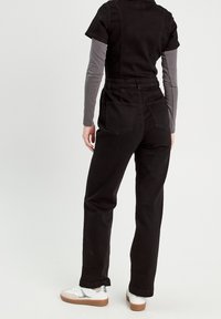 Černý džínový overal s krátkými rukávy a páskem zvýrazňujícím pas. Má dvě zadní kapsy, kombinovaný s šedými dlouhými rukávy a bílými teniskami.