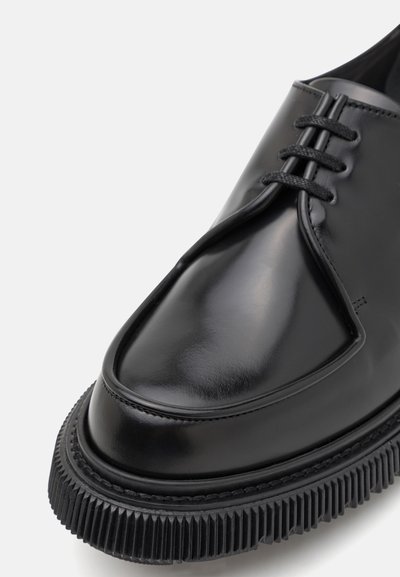 Black leather dress shoe with a glossy finish, lace-up design, rounded toe, and a textured rubber sole featuring ridges.