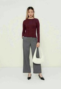 Top bordeaux de manga comprida com costuras frisadas, combinado com calças largas cinza às riscas e uma mala branca com detalhes em tachas. Sapatos de salto pretos e pontiagudos.