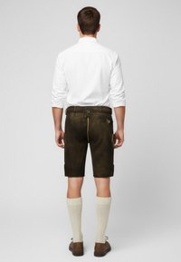 Pantaloni corti in pelle marrone con cordino in vita, tasche laterali e dettagli gialli, abbinati a calze lavorate a maglia color crema lunghe fino al ginocchio.
