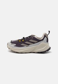 Chaussures de trail violettes et grises avec un dessus texturé, une semelle robuste offrant une traction prononcée, et un système de laçage rapide pour un maintien sécurisé.