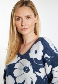 Woolmix trui met een marineblauwe achtergrond en grote witte bloemenpatronen, V-hals ontwerp en een zachte textuur.