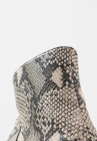 Botte à design montante, fabriquée en cuir synthétique effet python. Présente une surface texturée en noir et crème avec des motifs en losange.
