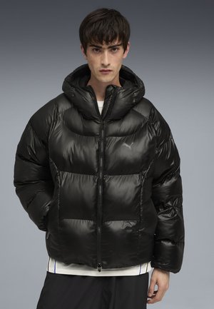 Giacca a vento nera con finitura lucida, cappuccio, chiusura con zip e design trapuntato. Presenta tasche laterali e un logo sul petto.