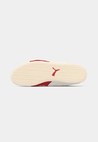 Sneaker rossa con suola testurizzata, con un'intermedia crema e un accento bianco. Il design include un logo in un colore a contrasto.