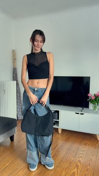 Top corto negro de tela transparente, jeans de mezclilla azul claro sueltos con dobladillos deshilachados y un bolso negro de hombro, todo ello sobre un fondo minimalista.
