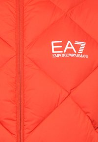 Rød pufferjakke med en diamant quiltet tekstur. Har en frontlynlås og et hvidt EA7 Emporio Armani-logo trykt på brystet.