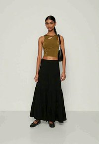 Ελιές πράσινη κοντό τοπ με κοπή, συνδυασμένο με μια μακριά μαύρη φούστα με επίπεδα. Μαύρα επίπεδα παπούτσια με καρφιά και μια μικρή μαύρη τσάντα.