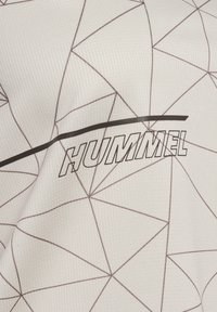 Tissu blanc avec de fines lignes géométriques noires et le mot « HUMMEL » imprimé en lettres capitales en contour avec une bande noire au-dessus.