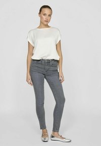 Top blanco de manga corta combinado con jeans gris ajustados y zapatos planos plateados. El diseño simple se centra en el minimalismo con texturas suaves.