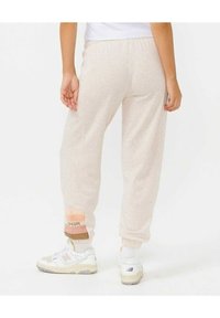 Ljust beige sweatshirtbyxor med avslappnad passform, med ribbade muddar i pastellfärger och en logotypdetalj på underbenet. Mjuk textur.