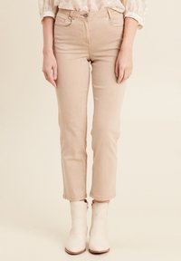 Beige cropped jeans met een slim fit silhouet, voorzien van vijf zakken en een knoopsluiting aan de voorkant. Gecombineerd met witte enkellaarsjes.