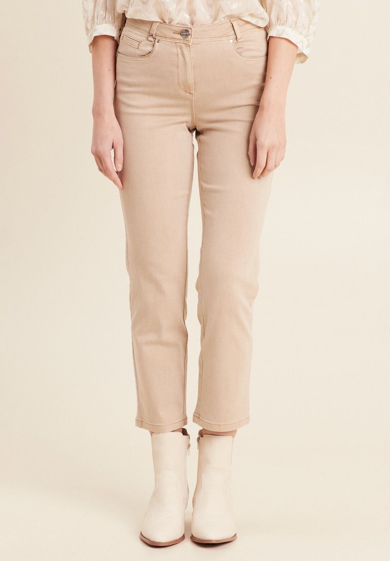 Beige cropped jeans met een slim fit silhouet, voorzien van vijf zakken en een knoopsluiting aan de voorkant. Gecombineerd met witte enkellaarsjes.