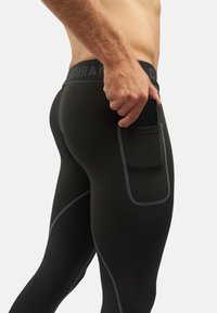 Sorte atletikleggings med tætsiddende design, udstyret med en sidelomme og kontrasterende grå syninger langs sømmene og taljebåndet.