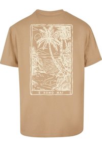 Kortærmet beige T-shirt har et cremefarvet palme-træ grafik og strandmotiv på bagsiden, med teksten "E KOMO MAI" nederst.