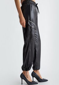 Sorte satin joggerbukser med elastisk talje, snøre detaljer, sidelommer med kontrastkant, kombineret med sorte dekorerede højhælede sko.