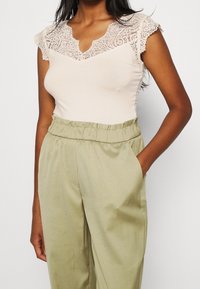 Jasnoróżowa bluzka z koronkowymi rękawami oraz falbaniastym dekoltem, w zestawieniu z oliwkowymi spodniami z wysokim stanem, posiadającymi boczne kieszenie.