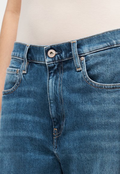 Blå jeans i denim med midjemått, försedd med knäppning, fem fickor och kontrasterande sömdetaljer.